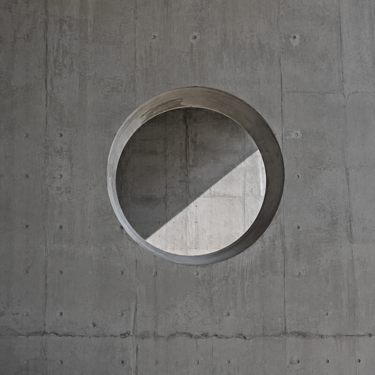 A circular oculus cut through raw concrete, daylight passing through.