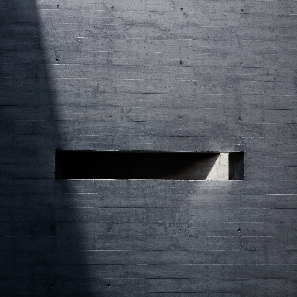A single slot opening in a massive concrete wall, receiving light.